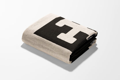 Folded tan throw blanket with a large black "E" initial.