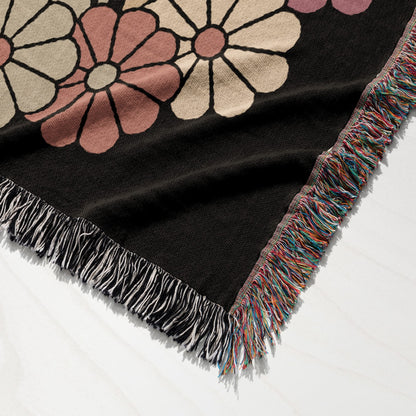 Black throw blanket with large pink and beige floral pattern and multicolored fringe.
