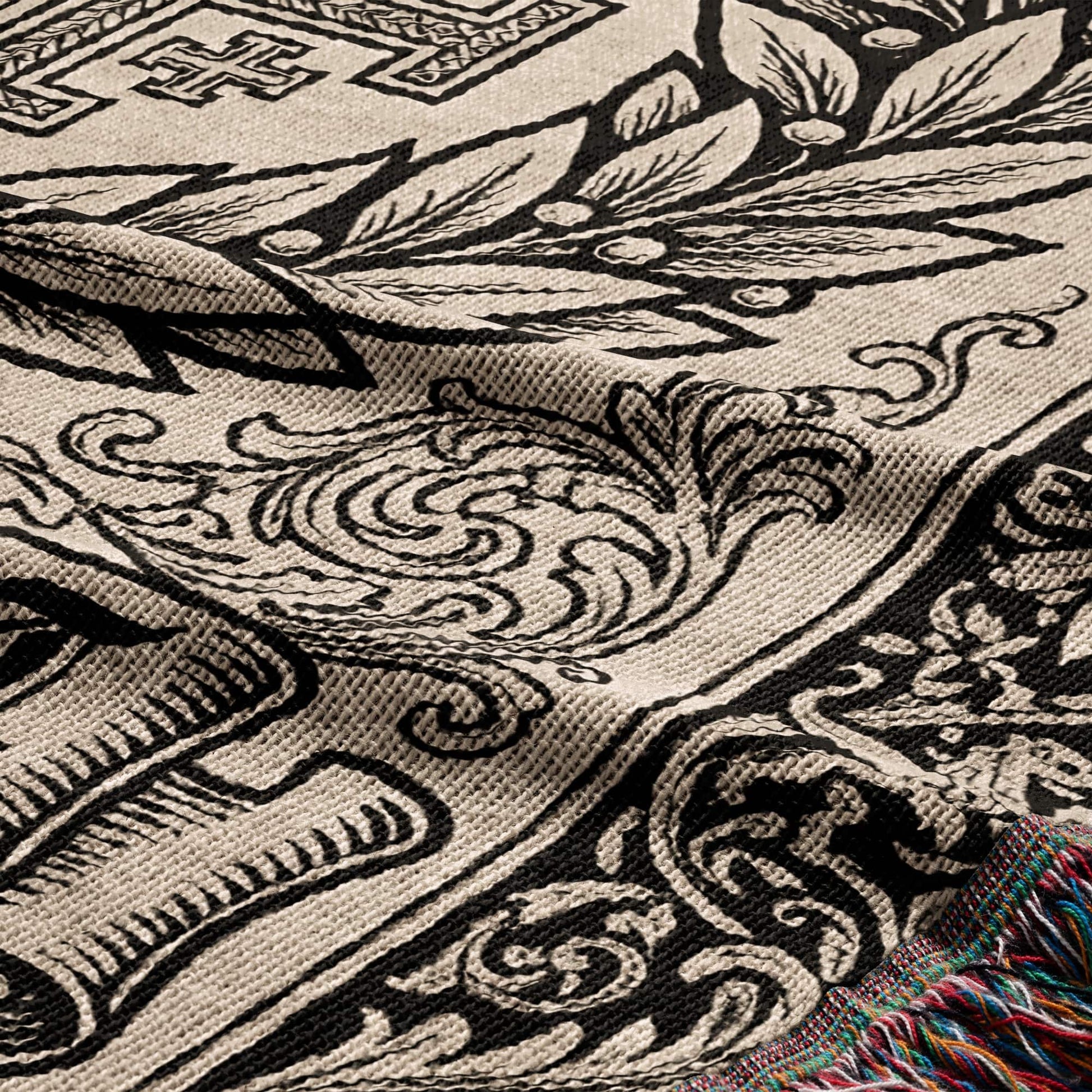 Woven blanket with black and beige ornate damask pattern and colorful fringed edge.