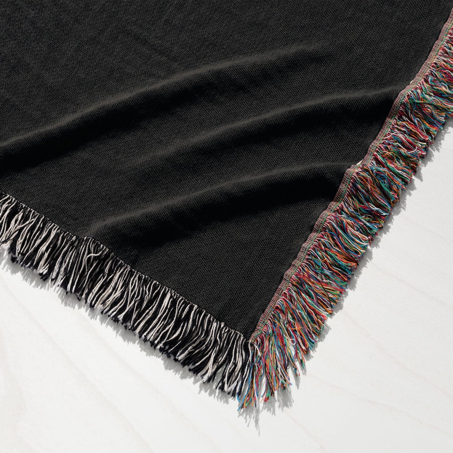 Black throw blanket with colorful fringe detail draped on white surface.
