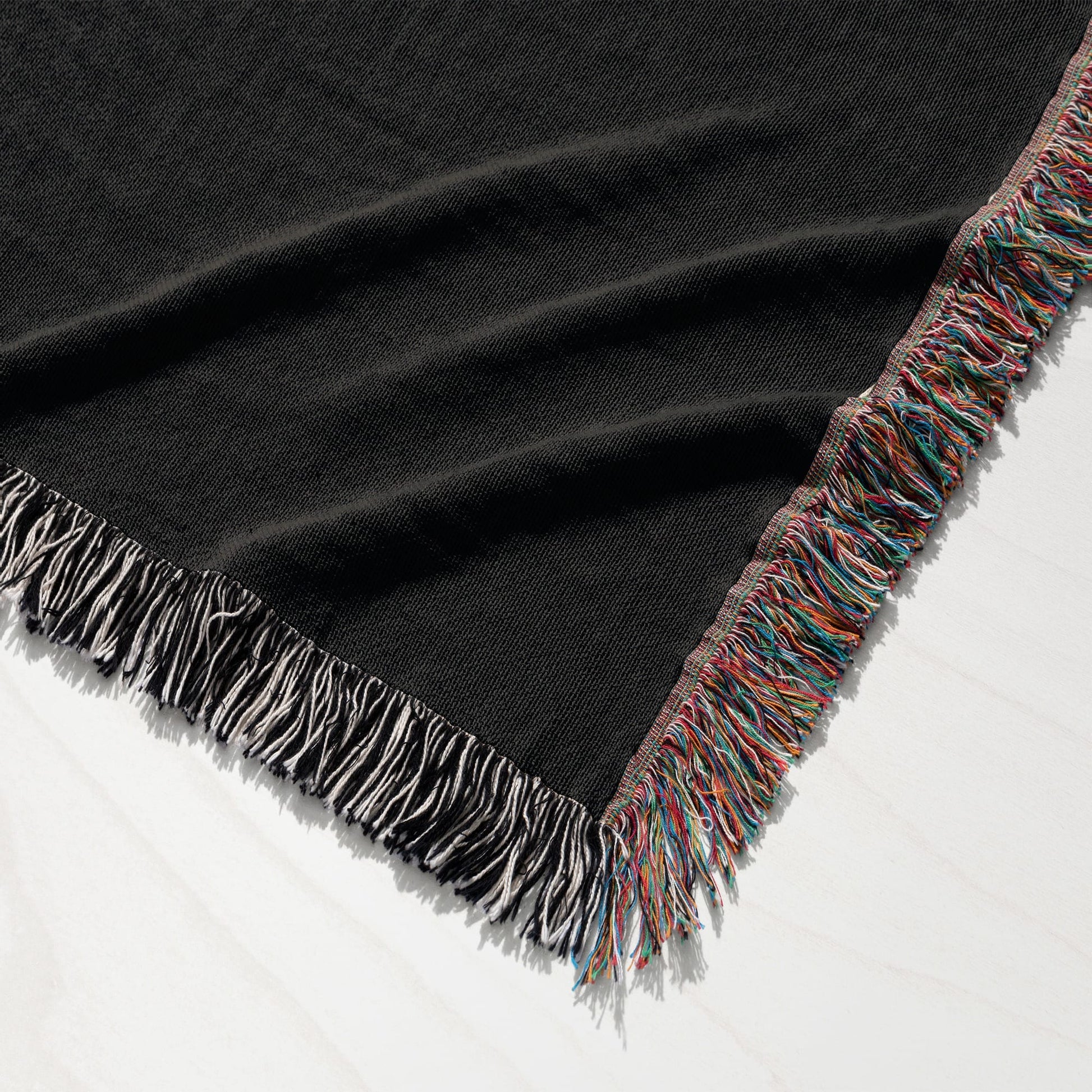 Black throw blanket with colorful fringe detail draped on white surface.