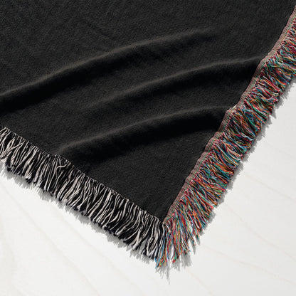 Black throw blanket with colorful fringe detail draped on white surface.