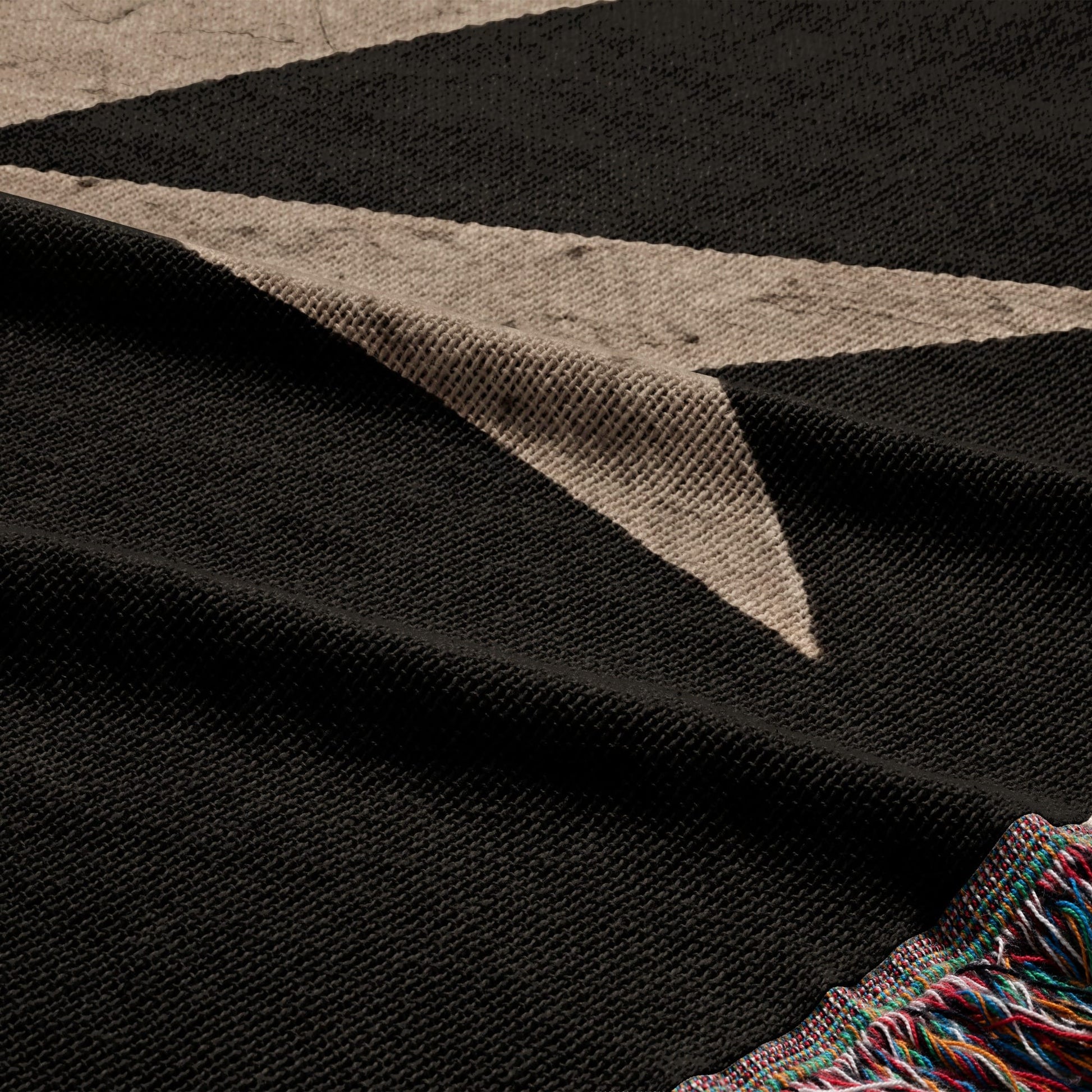 Black throw blanket with a muted beige geometric pattern and tasseled edge.