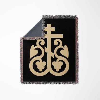 Black throw blanket with ornate beige cross design and fringed edges.