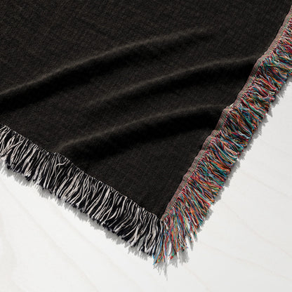 Black knit blanket with colorful fringed edges on a white wooden surface.