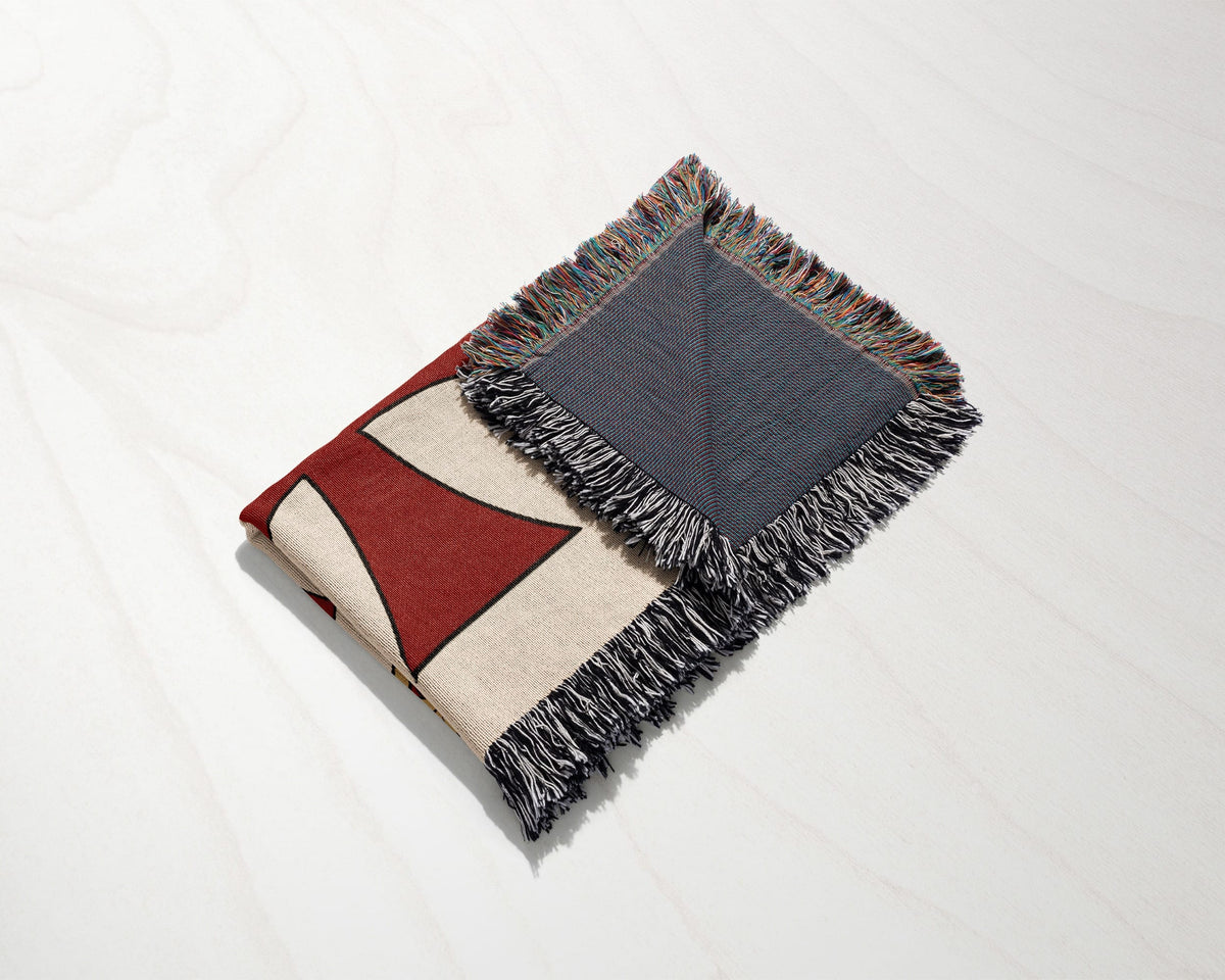 Woven blanket with geometric red and cream pattern and fringed edges.