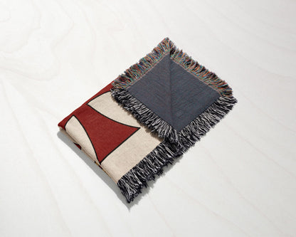 Woven blanket with geometric red and cream pattern and fringed edges.