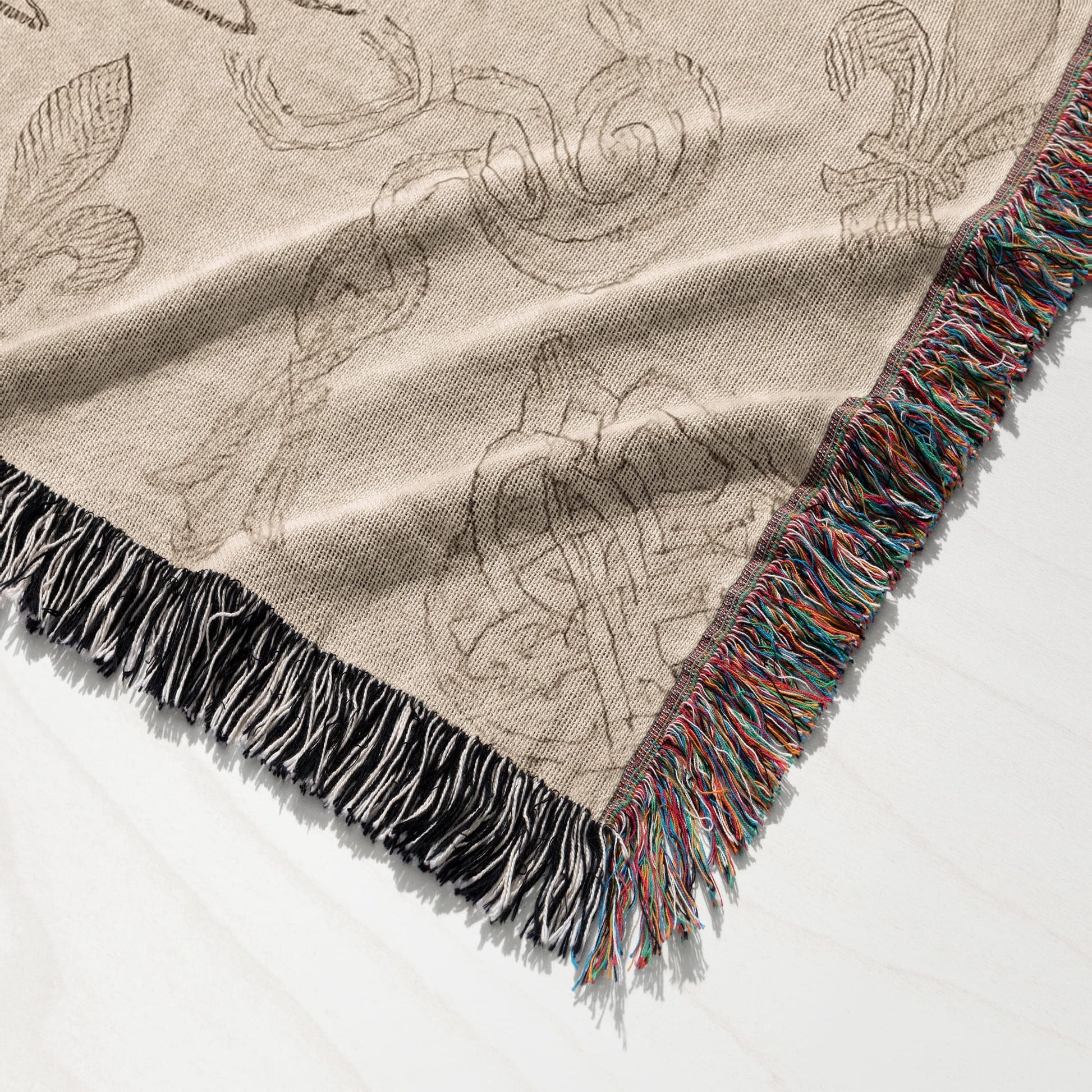Tan woven blanket with fringe and an abstract floral pattern.
