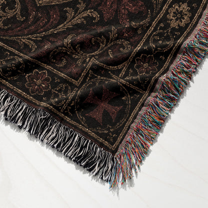 Woven tapestry blanket with intricate dark pattern and tasseled edges.