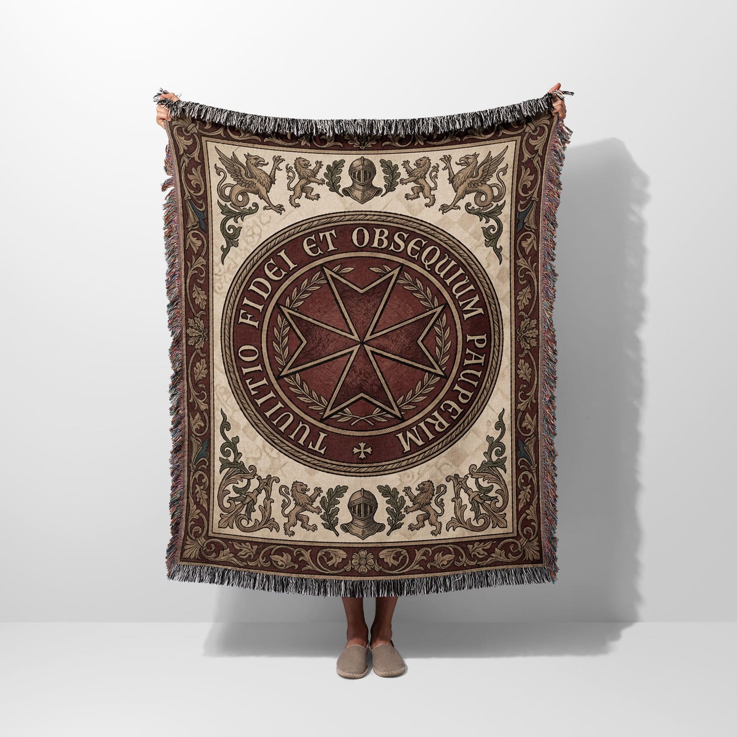 Tapestry blanket with Maltese cross and Latin inscription, held up by a person.