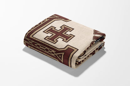 Folded blanket with a brown cross design on cream fabric.