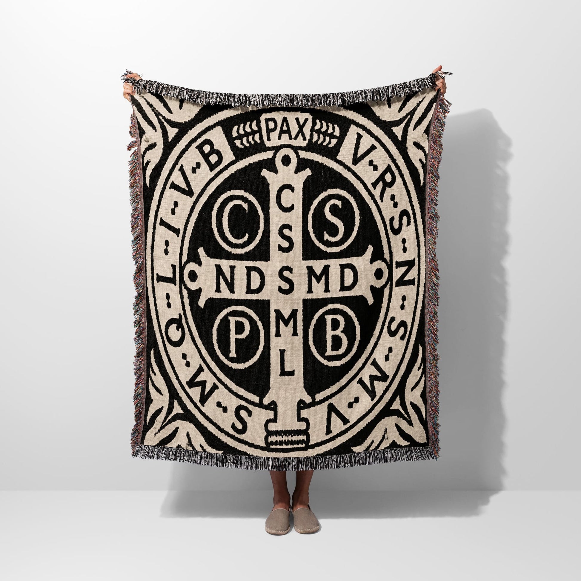 Black and tan woven throw with St. Benedict medal design and fringed edges.