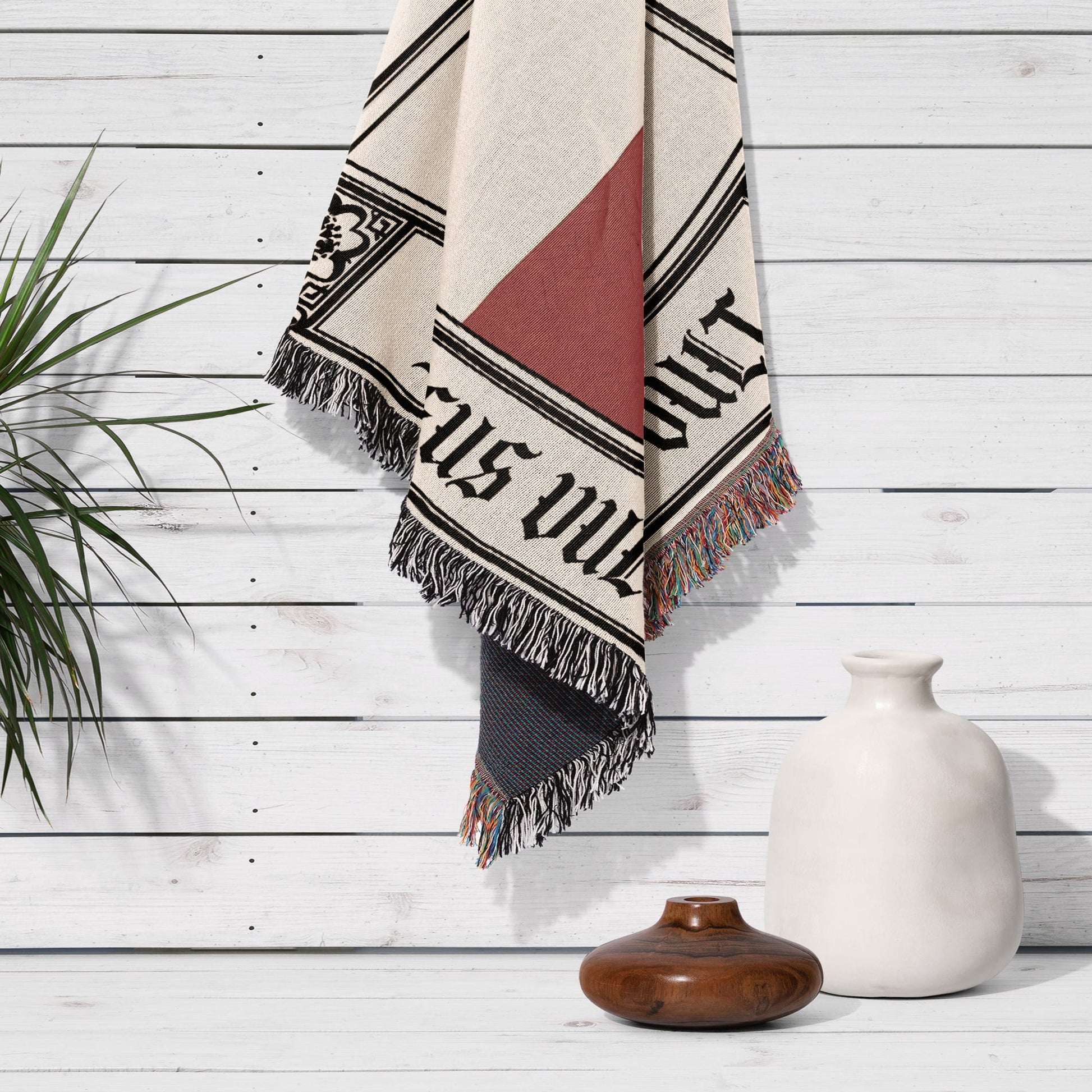 Woven blanket with black and red text hanging on a white wooden wall.