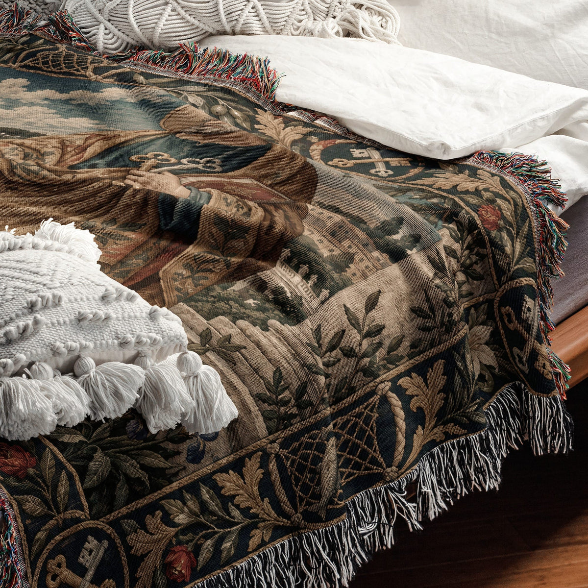 Woven tapestry throw blanket with a Renaissance art scene, floral border, and fringed edges on a bed.