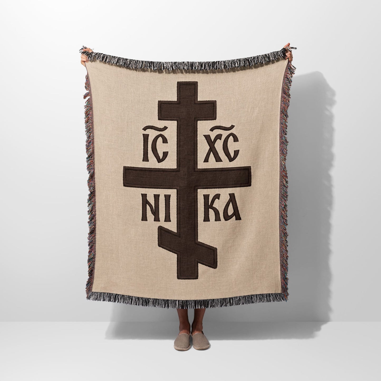 Brown Orthodox cross with IC XC NI KA inscription on beige woven blanket.