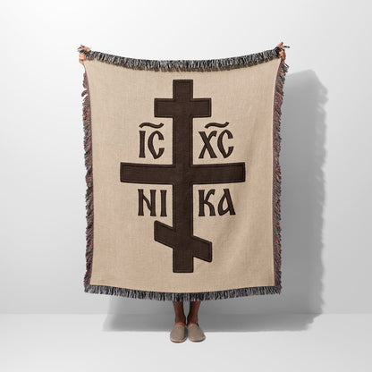 Brown Orthodox cross with IC XC NI KA inscription on beige woven blanket.