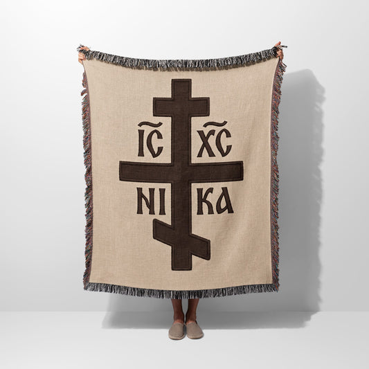 Brown Orthodox cross with IC XC NI KA inscription on beige woven blanket.