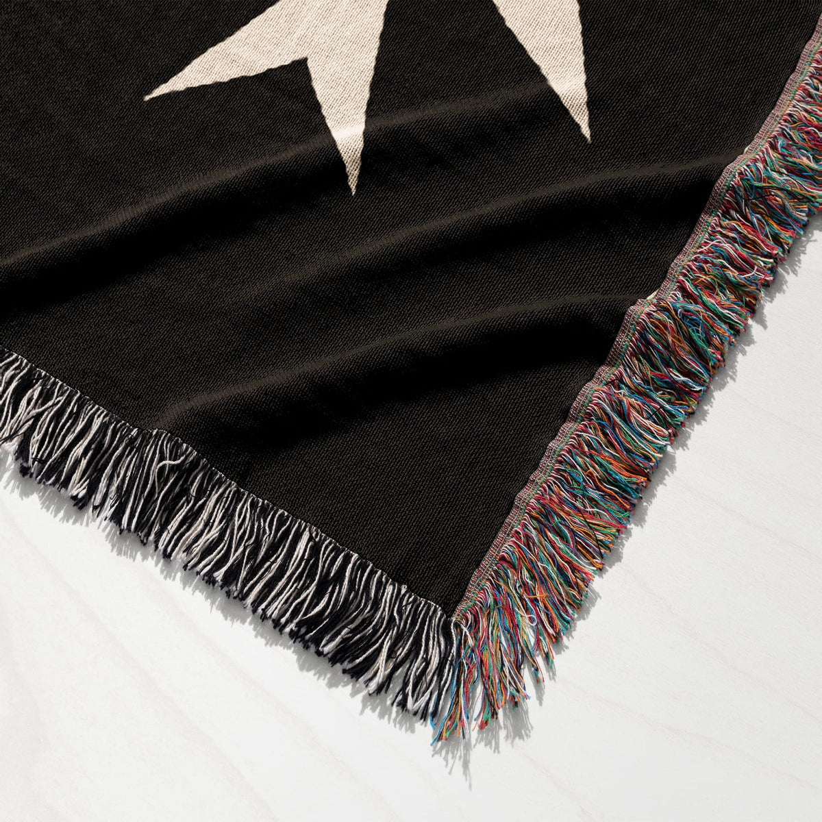 Black woven throw blanket with white stars and fringed edges.