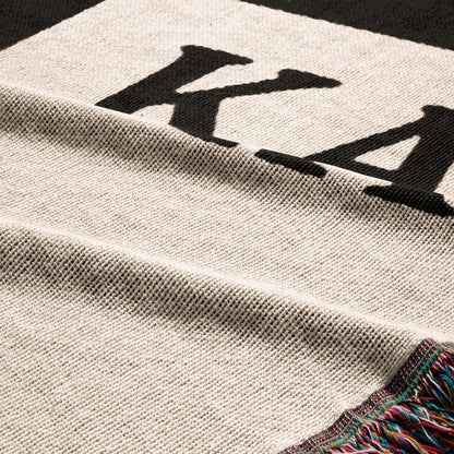 Cream knit blanket with black "KA" lettering and colorful fringe.