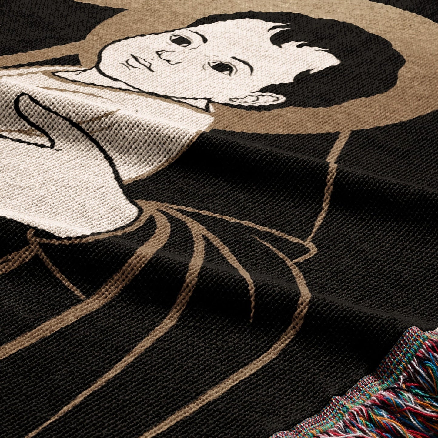Black knit blanket with a depiction of a face and hand, fringed edge.