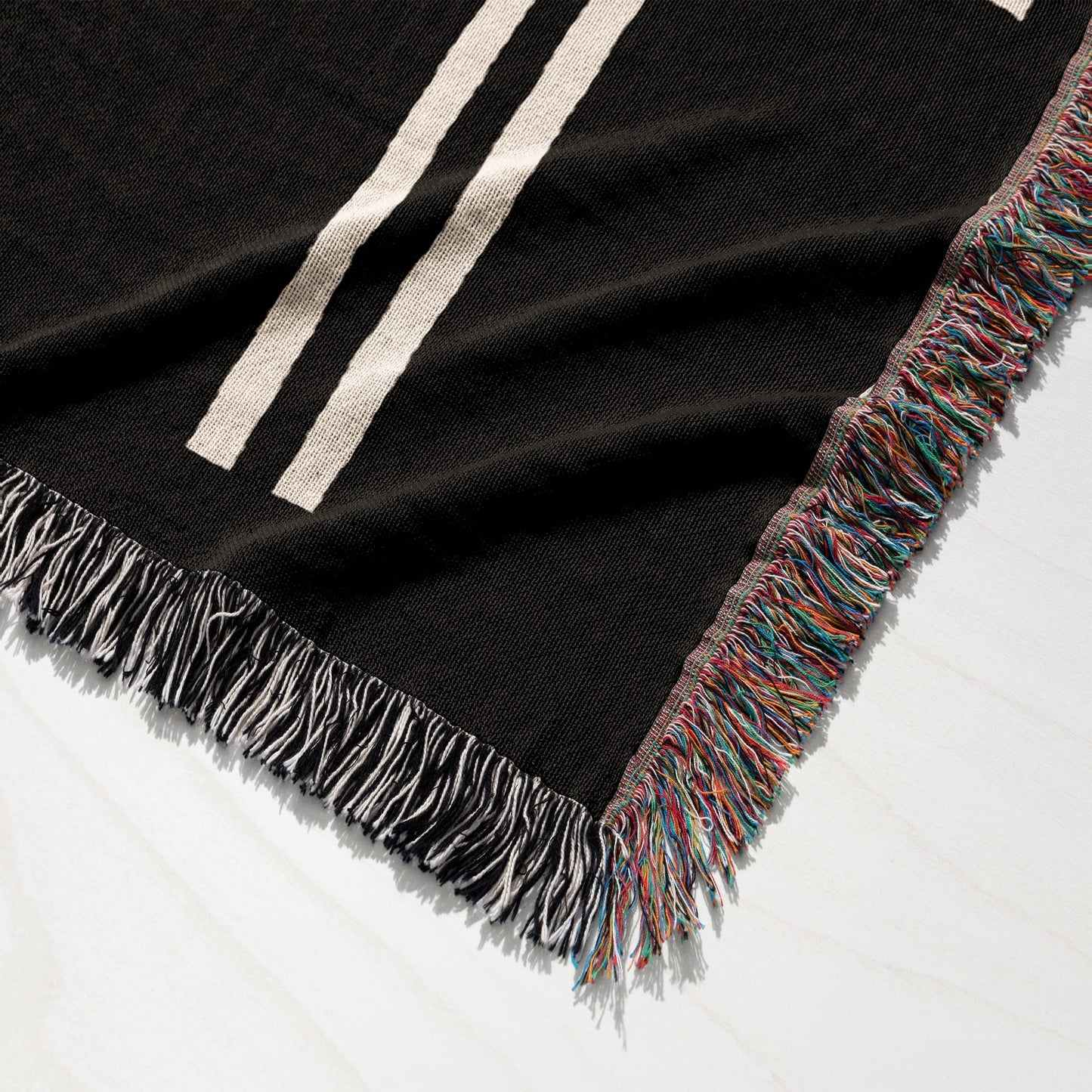 Black woven throw blanket with cream stripes and multicolor fringe.