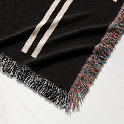 Black woven throw blanket with cream stripes and multicolor fringe.