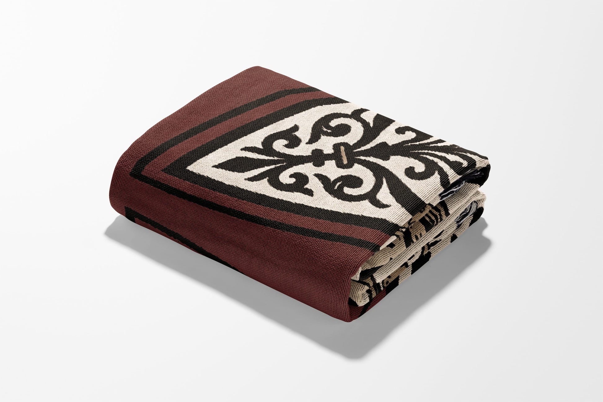 Folded burgundy throw blanket with black and cream ornate pattern on white background.