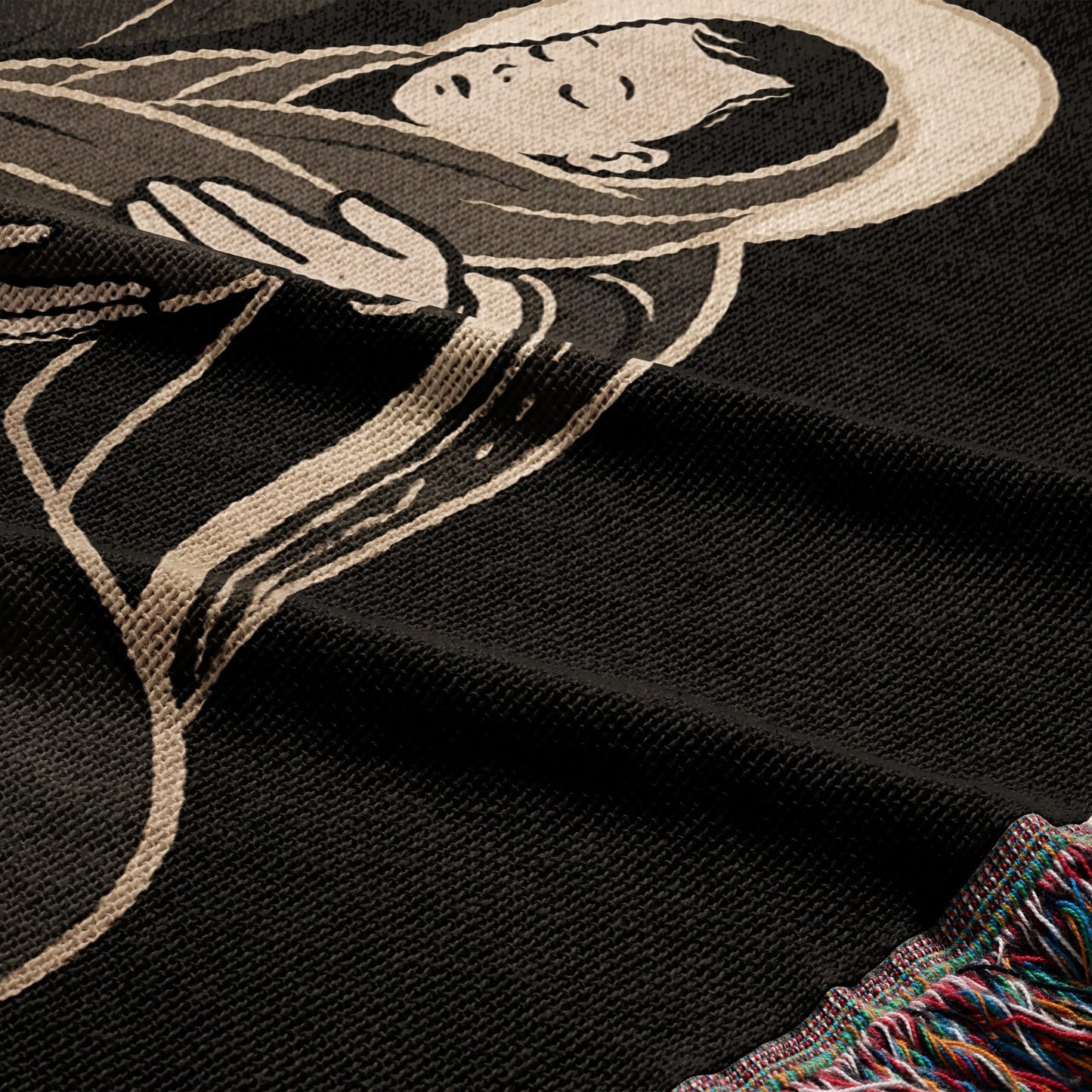 Black woven blanket with a depiction of a serene figure and colorful fringed edge.
