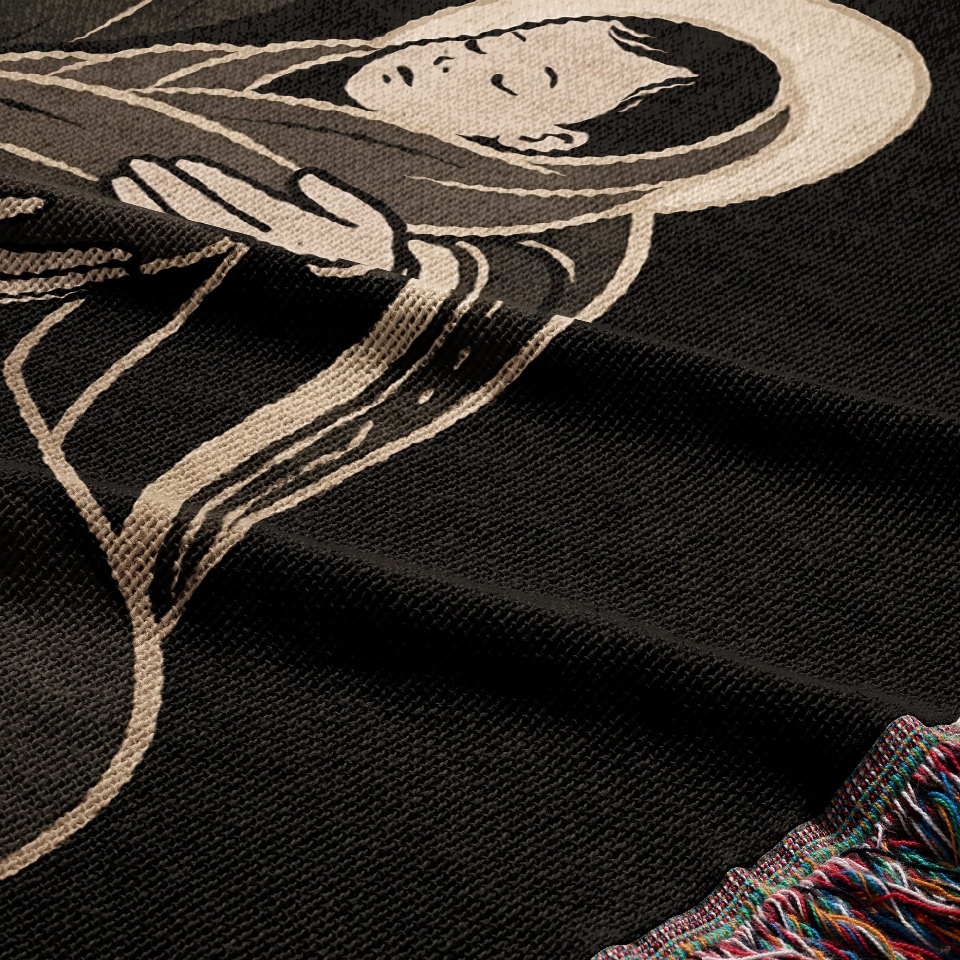 Black woven blanket with a depiction of a serene figure and colorful fringed edge.