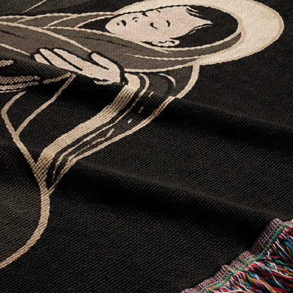 Black woven blanket with a depiction of a serene figure and colorful fringed edge.